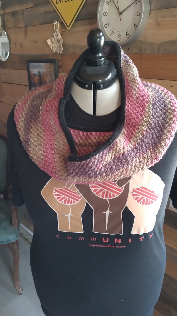 The purple, pink and gray cowl worked in seed stitch sits on a mannequin showing the swirling colors.