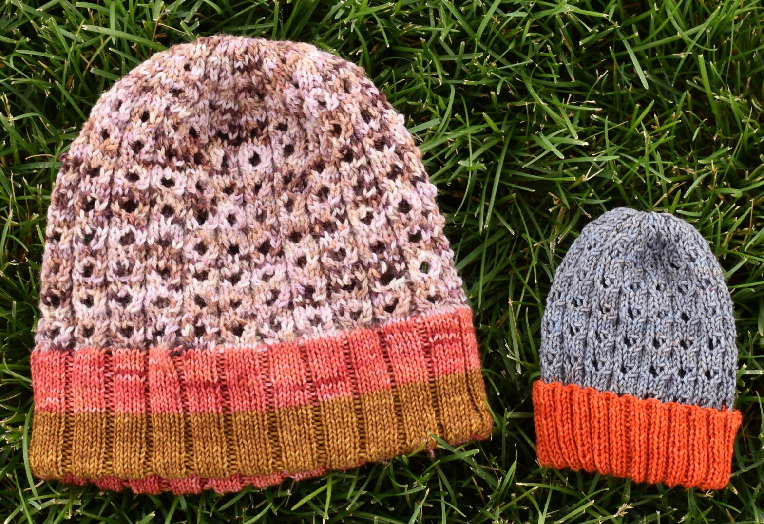 Two hats, one larger than the other, lay on the grass. The larger one is pink and brown, the smaller one is gray and orange.