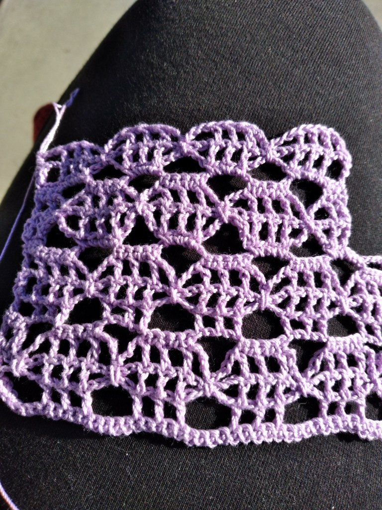 A small swatch of purple crochet lace sits on a black background.