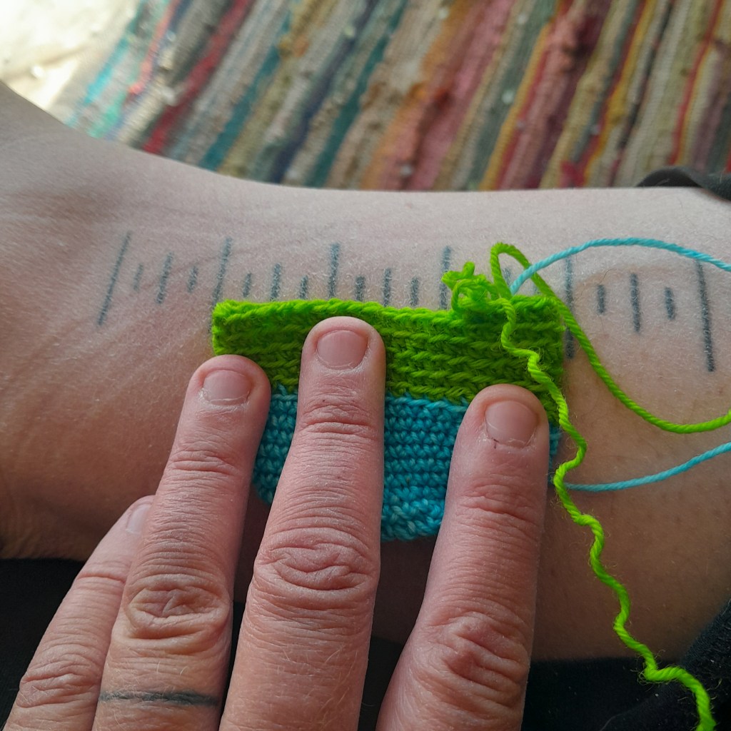 A partial sock is being measured using a ruler that has been tattooed on a leg. The sock is three inches wide.