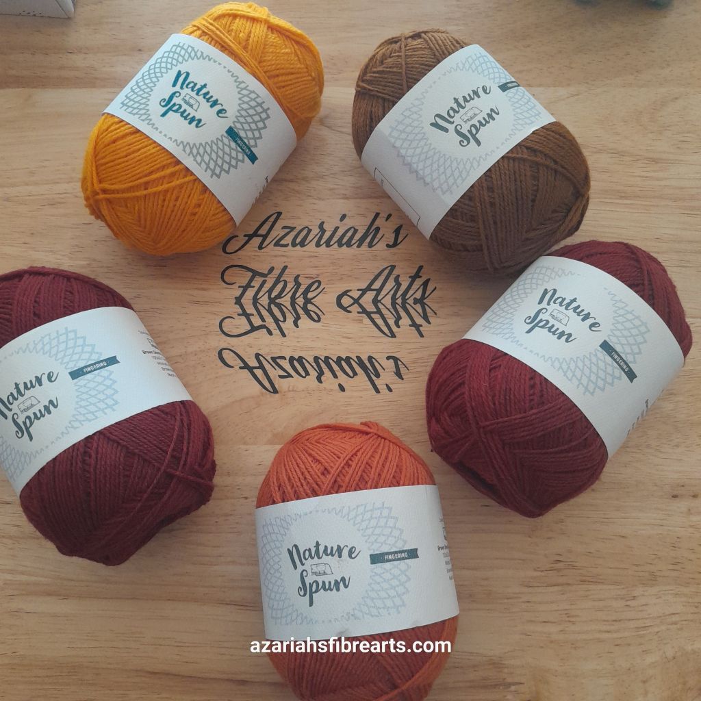 Five balls of yarn arranged in a rough circle on a brown background. The yarns are yellow, brown, yellow, orange and a couple shade of red. In the center of the circle is black script lettering in the middle that says "Azariah's Fibre Arts".